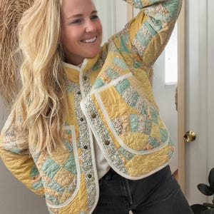 Puede incluir: Chaqueta acolchada con diseño de patchwork con patrones amarillos, azules y florales. La chaqueta tiene cuello redondo, cierre de botones y dos bolsillos delanteros. El ribete de la chaqueta es blanco con un diseño floral.