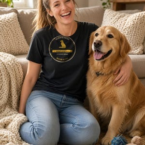 K&ouml;nnte beinhalten: Ein schwarzes T-Shirt mit einer kreisf&ouml;rmigen goldenen Grafik, die die Silhouette eines Hundes und den Text zeigt: GOLDEN RETRIEVER THERAPY DEPARTMENT NO APPOINTMENT NECESSARY WALK-INS WELCOME. Das T-Shirt wird mit einer hellblauen Jeans kombiniert.