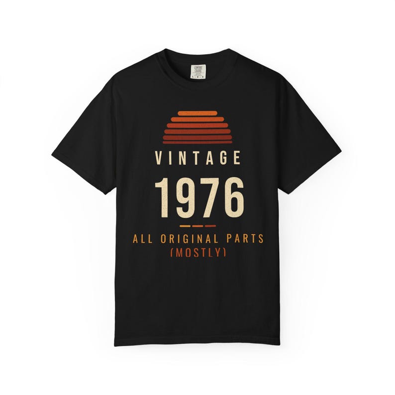 K&ouml;nnte beinhalten: Ein schwarzes Kurzarm-T-Shirt mit einer Grafik in Form eines Sonnenuntergangs in Orange- und Rott&ouml;nen. Der Text VINTAGE 1976 ALL ORIGINAL PARTS (MOSTLY) ist in cremefarbenen und orangen Buchstaben mittig aufgedruckt.