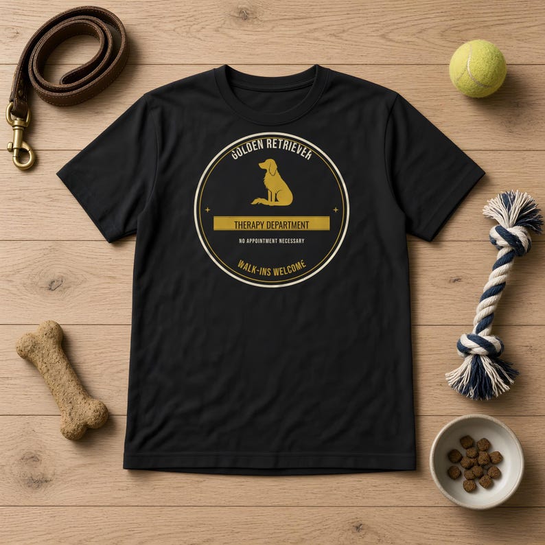 K&ouml;nnte beinhalten: Ein schwarzes Kurzarm-T-Shirt mit einem kreisf&ouml;rmigen Aufdruck, der die Silhouette eines Golden Retrievers zeigt. Der Text lautet: GOLDEN RETRIEVER, THERAPY DEPARTMENT, NO APPOINTMENT NECESSARY, WALK-INS WELCOME. Das Design ist in Gold und Wei&szlig; gedruckt.