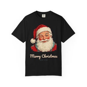 May include: A black short-sleeve t-shirt featuring a graphic of a winking Santa Claus in a red hat and white beard. Below the graphic, the text reads Merry Christmas, followed by smaller text that says NORTH POLE EST. 1825.