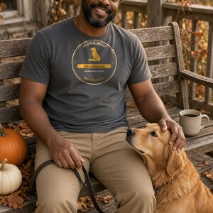K&ouml;nnte beinhalten: Ein anthrazitfarbenes Kurzarm-T-Shirt mit einer kreisf&ouml;rmigen goldenen Grafik, die die Silhouette eines Hundes und den Text Golden Retriever Therapy Department No Appointment Necessary Walk-ins Welcome zeigt.
