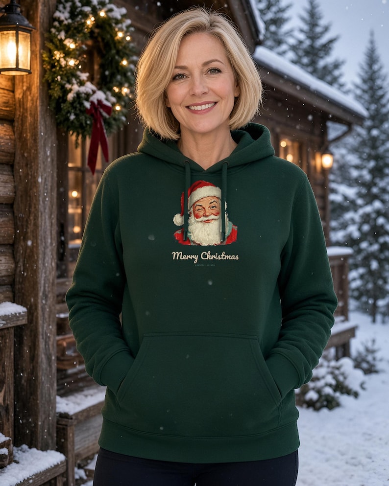 May include: A dark green hooded sweatshirt featuring a graphic of a winking Santa Claus wearing a red hat and white beard, with the text Merry Christmas printed in a cream-colored script font centered below the illustration.