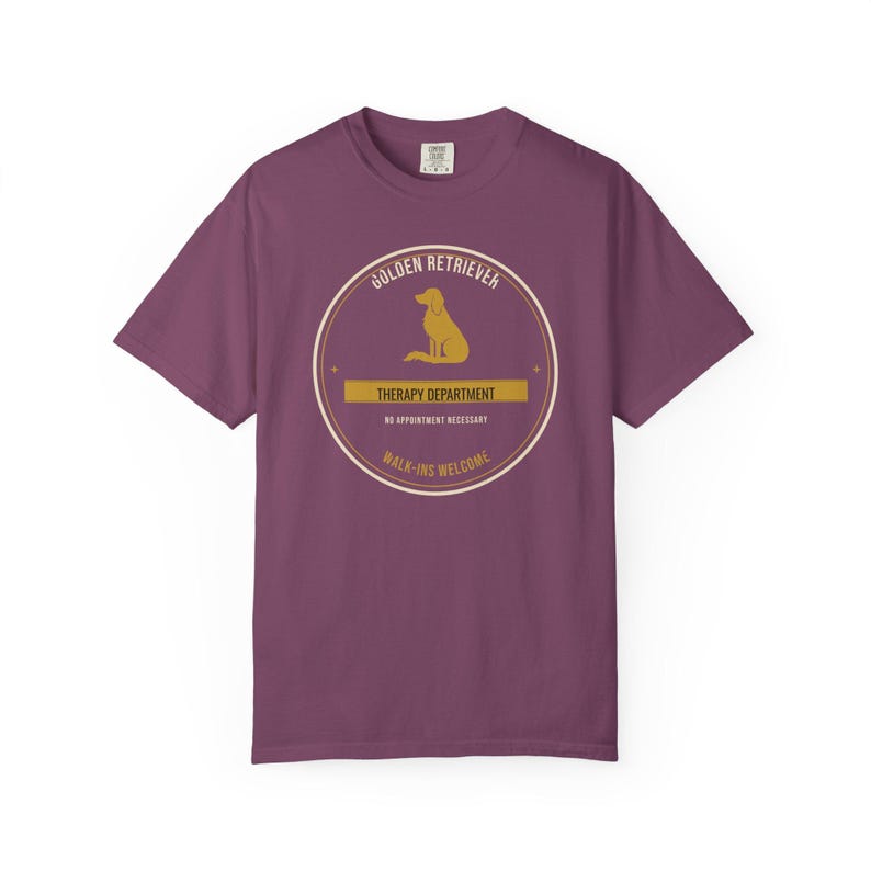 K&ouml;nnte beinhalten: Ein pflaumenfarbenes Kurzarm-T-Shirt mit einer kreisf&ouml;rmigen Grafik, die die Silhouette eines Golden Retrievers zeigt. Der Text lautet: GOLDEN RETRIEVER, THERAPY DEPARTMENT, NO APPOINTMENT NECESSARY und WALK-INS WELCOME in Creme und Gold.