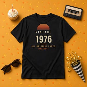 K&ouml;nnte beinhalten: Ein schwarzes Kurzarm-T-Shirt mit einer Grafik, die ein Sonnenuntergangsdesign, den Text VINTAGE 1976 und die Worte ALL ORIGINAL PARTS (MOSTLY) in wei&szlig;er und orangefarbener Schrift auf der Vorderseite zeigt.
