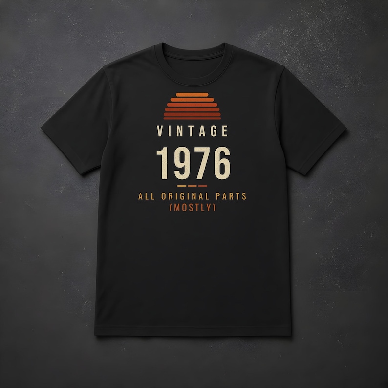 K&ouml;nnte beinhalten: Ein schwarzes Kurzarm-T-Shirt mit einem Grafikdruck in Form eines Sonnenuntergangs in Orange- und Rott&ouml;nen. Der Text VINTAGE 1976 ALL ORIGINAL PARTS (MOSTLY) ist in wei&szlig;er und oranger Schrift mittig auf der Brust platziert.