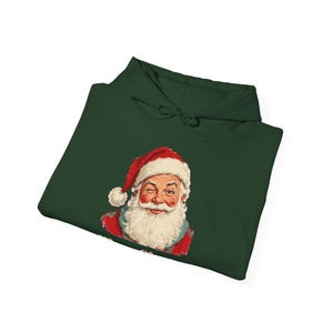 May include: A dark forest green hooded sweatshirt featuring a graphic illustration of a winking Santa Claus wearing a red hat with a white pom-pom and a white beard. The hoodie includes a drawstring hood and long sleeves in a solid color.