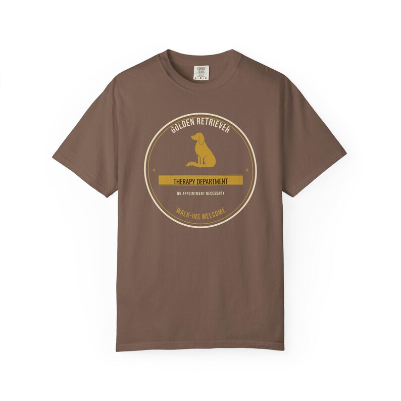 K&ouml;nnte beinhalten: Ein braunes Kurzarm-T-Shirt mit einer kreisf&ouml;rmigen Grafik, die die Silhouette eines Golden Retrievers zeigt. Der Text lautet: GOLDEN RETRIEVER, THERAPY DEPARTMENT, NO APPOINTMENT NECESSARY, WALK-INS WELCOME. Das Design ist mittig platziert.