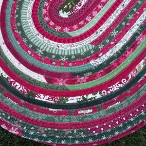 May include: A red and green oval rug made of fabric scraps sewn together in a circular pattern. The rug has a Christmas theme with snowflakes, trees, and other holiday motifs.