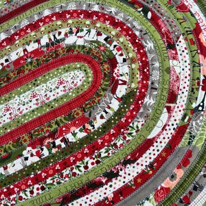May include: A red, green, and white oval rug with a Christmas theme. The rug is made of fabric strips sewn together in a circular pattern. The fabric strips have various Christmas-themed prints, including snowflakes, stars, and Christmas trees.