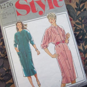 May include: A vintage sewing pattern titled "Style" with a teal dress and a pink striped dress illustration. The pattern size is N, for sizes 10, 12, and 14. The background features a floral fabric.