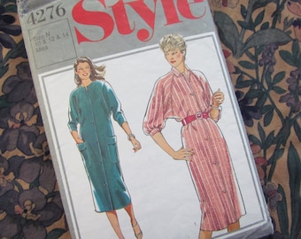 May include: A vintage sewing pattern titled "Style" with a teal dress and a pink striped dress illustration. The pattern size is N, for sizes 10, 12, and 14. The background features a floral fabric.
