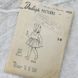 May include: Vintage sewing pattern for a girl's dress, size 6-7, from Druleigh Patterns. The pattern is for a sleeveless dress with a gathered skirt and lace edging. The pattern is printed on a cream-colored paper with black ink.