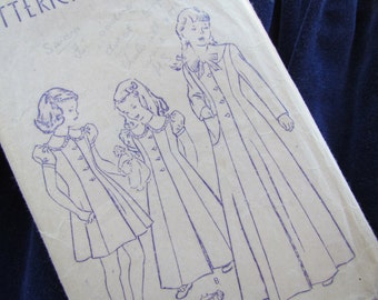 May include: Vintage sewing pattern for a girls' dress and coat. The pattern includes three different sizes: a small dress, a larger dress, and a coat. The pattern is printed on white paper with blue ink.