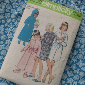 May include: Simplicity sewing pattern for children's robes. The pattern shows four girls wearing different robes, including a blue robe, a pink robe, a floral robe, and a white robe. The pattern is for size 4, with a 58 cm chest.