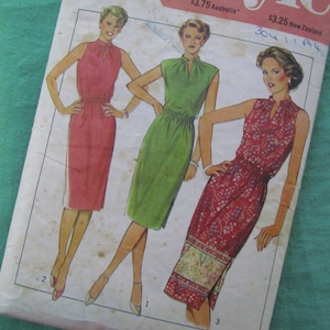 May include: Vintage sewing pattern featuring illustrations of three dresses. The dresses are in shades of red, green, and a floral print. Each dress has a high neckline and a fitted waist. The pattern is on a slightly aged paper.