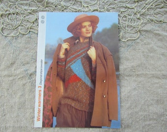 May include: A woman wearing a brown coat over a brown, blue, and red diagonal stripe sweater. She is wearing a brown hat and has brown hair. The text "Winter warmers 3 Diagonal stripe sweater" is printed on the side of the image.