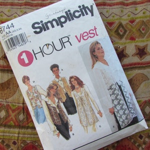 Puede incluir: Patrón de costura Simplicity número 8744 para un chaleco. El patrón se titula "1 HOUR vest" y presenta un chaleco blanco con detalles de encaje. El patrón incluye instrucciones para hacer cuatro estilos diferentes de chalecos.