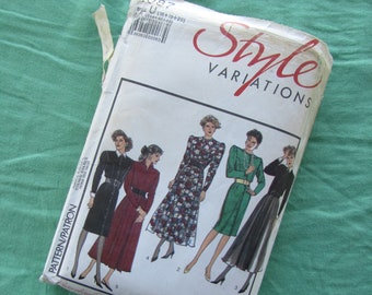 May include: A vintage sewing pattern titled "Style Variations" featuring illustrations of five different dress designs. The pattern envelope is white with red lettering and is set against a green fabric background.