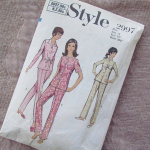 May include: Vintage sewing pattern for a pajama set. The pattern is for a size 12 with a bust of 34 inches and a waist of 25 1/2 inches. The pattern shows three different styles of pajamas, one with a floral print, one with a solid pink color, and one with a plaid pattern.
