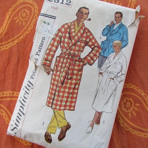 May include: Vintage Simplicity sewing pattern for a men's robe. The pattern is for a robe with a plaid pattern and a white robe. The pattern is labelled "Simplicity Printed Pattern" and "Small".