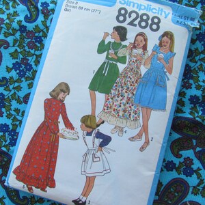May include: A vintage Simplicity sewing pattern, number 8288, featuring illustrations of girls in dresses. The pattern includes measurements for a size 8 girl, with a breast size of 27 inches. The background includes a paisley patterned fabric.