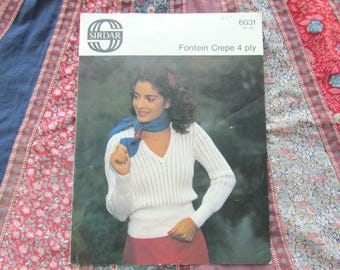 May include: Vintage Sirdar knitting pattern featuring a woman wearing a white V-neck sweater with vertical stripes, a blue scarf, and a red skirt. The pattern is titled "Fountain Crepe 4 ply."