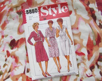 May include: A vintage sewing pattern titled "Style 3850" featuring illustrations of three dresses. The pattern is for sizes 0, 12, 14, and 16. The background is a colorful fabric with abstract floral patterns in shades of red, pink, and white.