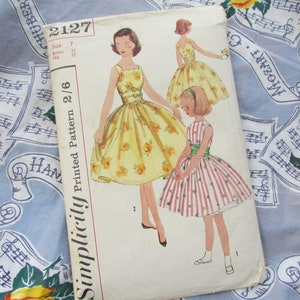 Puede incluir: Patrón de costura Simplicity impreso 2/6, número de patrón 2127, talla 7, pecho 25, cadera 27. El patrón incluye instrucciones para hacer dos vestidos, uno con estampado floral amarillo y otro con estampado de rayas rojas y blancas.