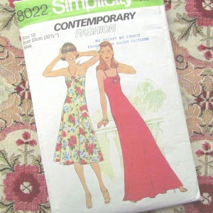 Puede incluir: Patrón de costura Simplicity 8022 para moda contemporánea. El patrón presenta ilustraciones de dos vestidos: un vestido floral con cuello halter y un vestido rojo con tirantes finos. El patrón es talla 10, contorno de busto 83cm.