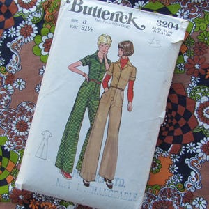 Peut inclure: Patron de couture Butterick vintage, taille 8, avec des illustrations de deux femmes en combinaisons. L'enveloppe indique "Butterick THE FASHION ONE" et "BUST 31 1/2". Le fond est un tissu floral coloré.