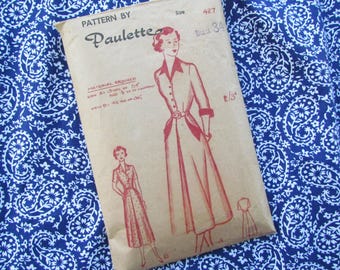 May include: A vintage sewing pattern by Paulette, size 427, featuring a dress illustration. The pattern is on a tan paper background, with text indicating material requirements. The background is a blue fabric with a white paisley pattern.