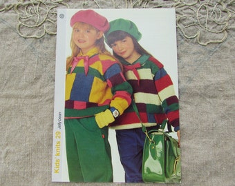 May include: A pattern booklet titled Kids' knits 29 Jelly bean featuring two children wearing colorful block-patterned knit sweaters, berets in pink and green, and solid-colored trousers. One child wears a green satchel with a gold buckle.