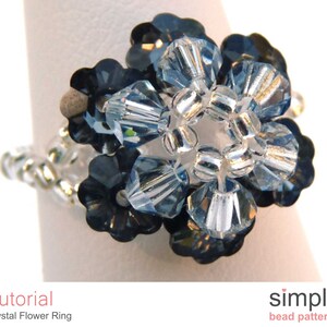 May include: A silver ring with a blue crystal flower design. The flower is made of small, faceted crystals in shades of blue and clear. The ring is a simple and elegant piece of jewelry.