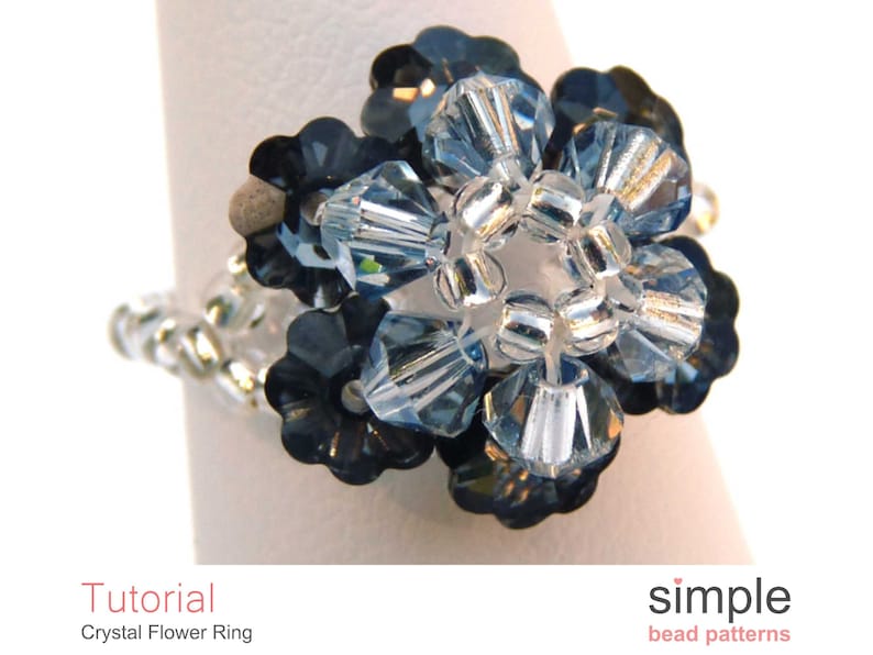 May include: A silver ring with a blue crystal flower design. The flower is made of small, faceted crystals in shades of blue and clear. The ring is a simple and elegant piece of jewelry.