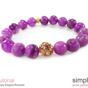 Op de afbeelding: Een armband van paarse edelstenen met een gouden en roze kristallen kralenbedel. De armband is gemaakt met ronde, gladde kralen.