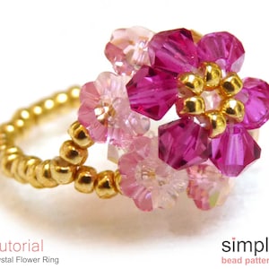 May include: A gold ring with a pink and purple crystal flower design. The ring is made with small gold beads and features a crystal flower with a pink center and purple petals.