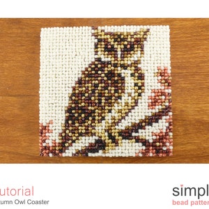May include: A beaded owl coaster featuring brown, gold and white beads. The owl is perched on a branch with red and gold beads. The coaster is on a wooden surface.