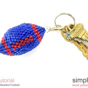 May include: A blue and red beaded football keychain. The football is attached to a silver key ring with a silver clasp. The keychain is hanging from a set of keys.