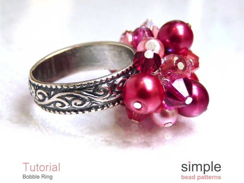 Może przedstawiać: Srebrny pierścionek z ozdobnym wzorem i gromadą r&oacute;żowych i czerwonych koralik&oacute;w. Korale są połączeniem kształt&oacute;w okrągłych i fasetowanych.