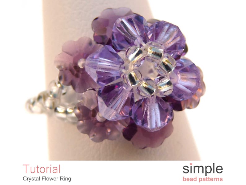 May include: A purple crystal flower ring with silver beads. The ring is made with small, faceted crystals that are arranged in a flower shape. The ring is a delicate and feminine piece of jewelry.