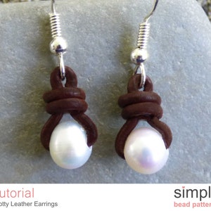 May include: A pair of brown leather earrings with a pearl accent. The earrings are knotted and have a silver hook fastening. The earrings are on a grey background.
