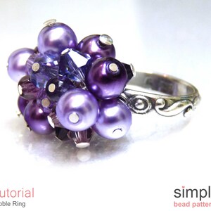 Może przedstawiać: Pierścionek w kolorze fioletowym i srebrnym z gromadą koralik&oacute;w. Pierścionek wykonany jest z małych fioletowych i srebrnych koralik&oacute;w, a obrączka jest srebrna z ozdobnym wzorem.