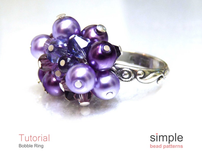 Może przedstawiać: Pierścionek w kolorze fioletowym i srebrnym z gromadą koralik&oacute;w. Pierścionek wykonany jest z małych fioletowych i srebrnych koralik&oacute;w, a obrączka jest srebrna z ozdobnym wzorem.