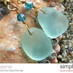 May include: A pair of sea glass earrings with gold wire and blue crystal accents. The sea glass is a light blue color and is shaped like a teardrop. The earrings are hanging from a gold wire.