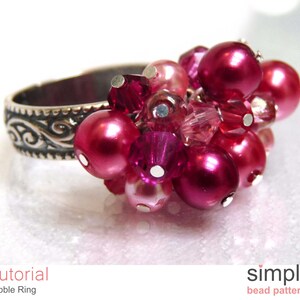 Może przedstawiać: Srebrny pierścionek z gromadą r&oacute;żowych i czerwonych koralik&oacute;w. Pierścionek ma ozdobny wz&oacute;r na obrączce.