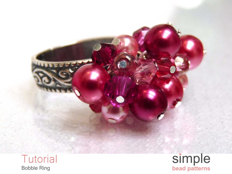 Może przedstawiać: Srebrny pierścionek z gromadą r&oacute;żowych i czerwonych koralik&oacute;w. Pierścionek ma ozdobny wz&oacute;r na obrączce.