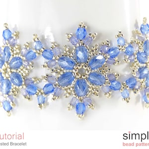 Può includere: Un primo piano di un braccialetto di perline blu e argento con un motivo a fiocco di neve. Il braccialetto è realizzato con perline piccole e rotonde ed è un gioiello delicato. Il testo "Tutorial Frosted Bracelet" è visibile nella parte inferiore dell'immagine.