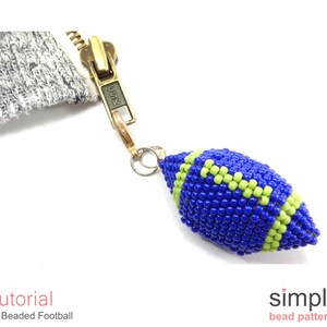 May include: A blue and green beaded football charm with a gold zipper pull attached. The charm is a 3D beaded design and is a great addition to a bag or keychain.