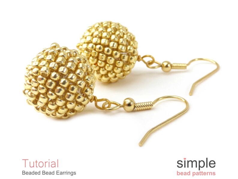May include: A pair of gold beaded earrings with a spherical design. The earrings are made with small, round beads that are tightly packed together to create a smooth, rounded shape. The earrings are attached to gold hooks.